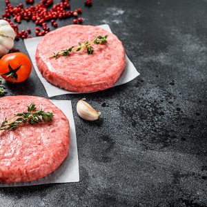 Burger patties, raw fresh ground, mince meat. Black background.